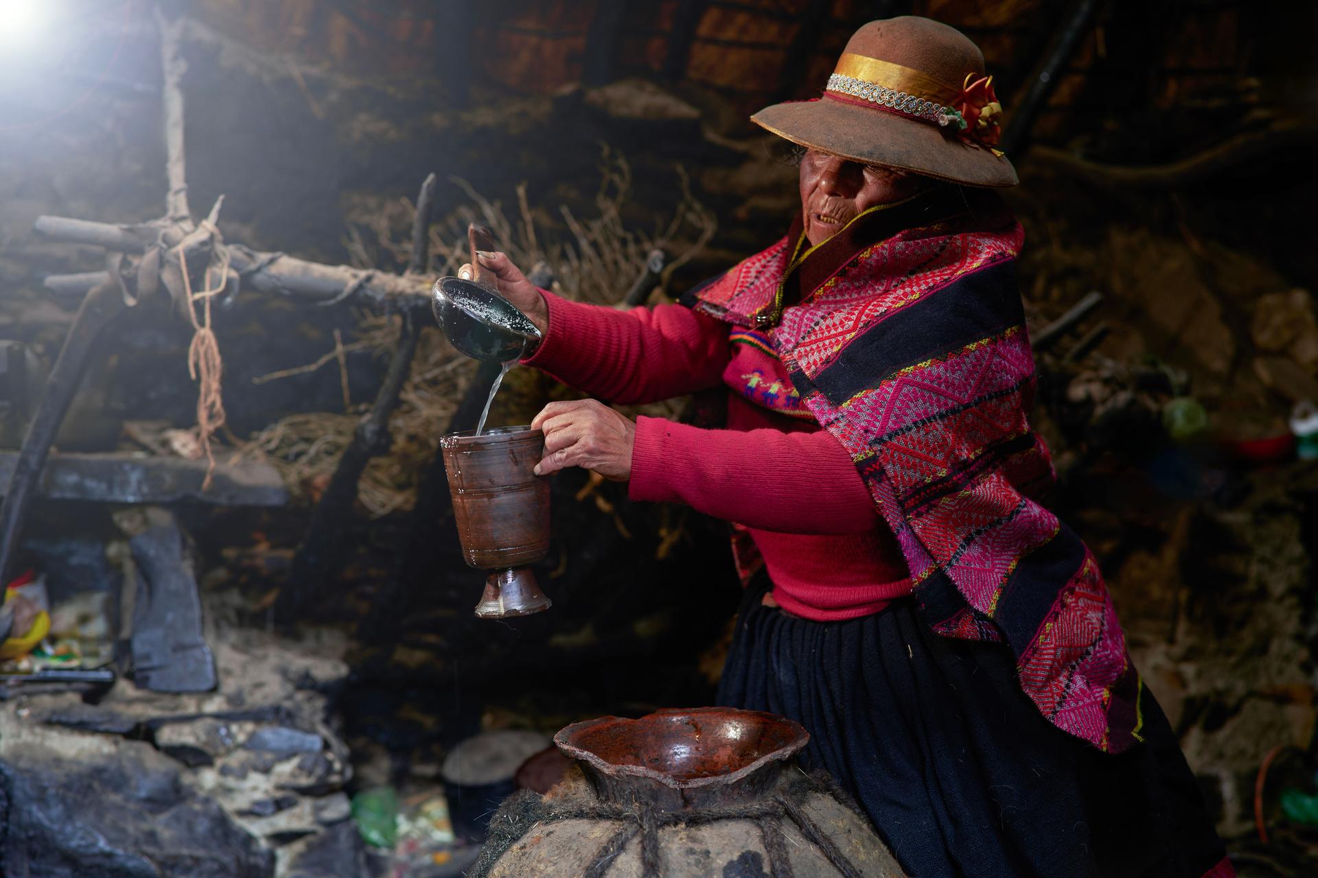 Woman from the Quechua Quero ethnic group pours a sacred and typical drink from the Andes called chica into a clay glass.